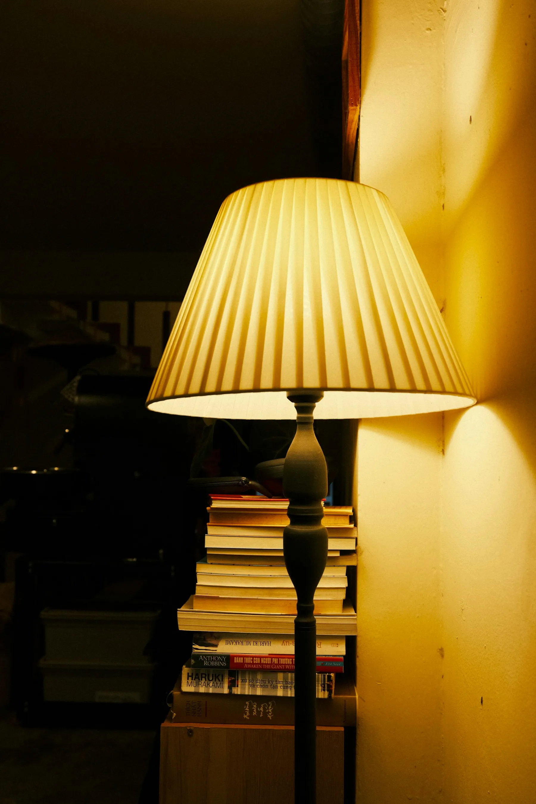 A lit table lamp beside a stack of books in a dark room