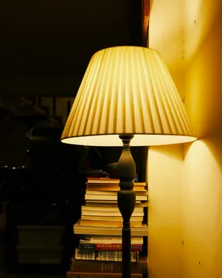 A lit table lamp beside a stack of books in a dark room