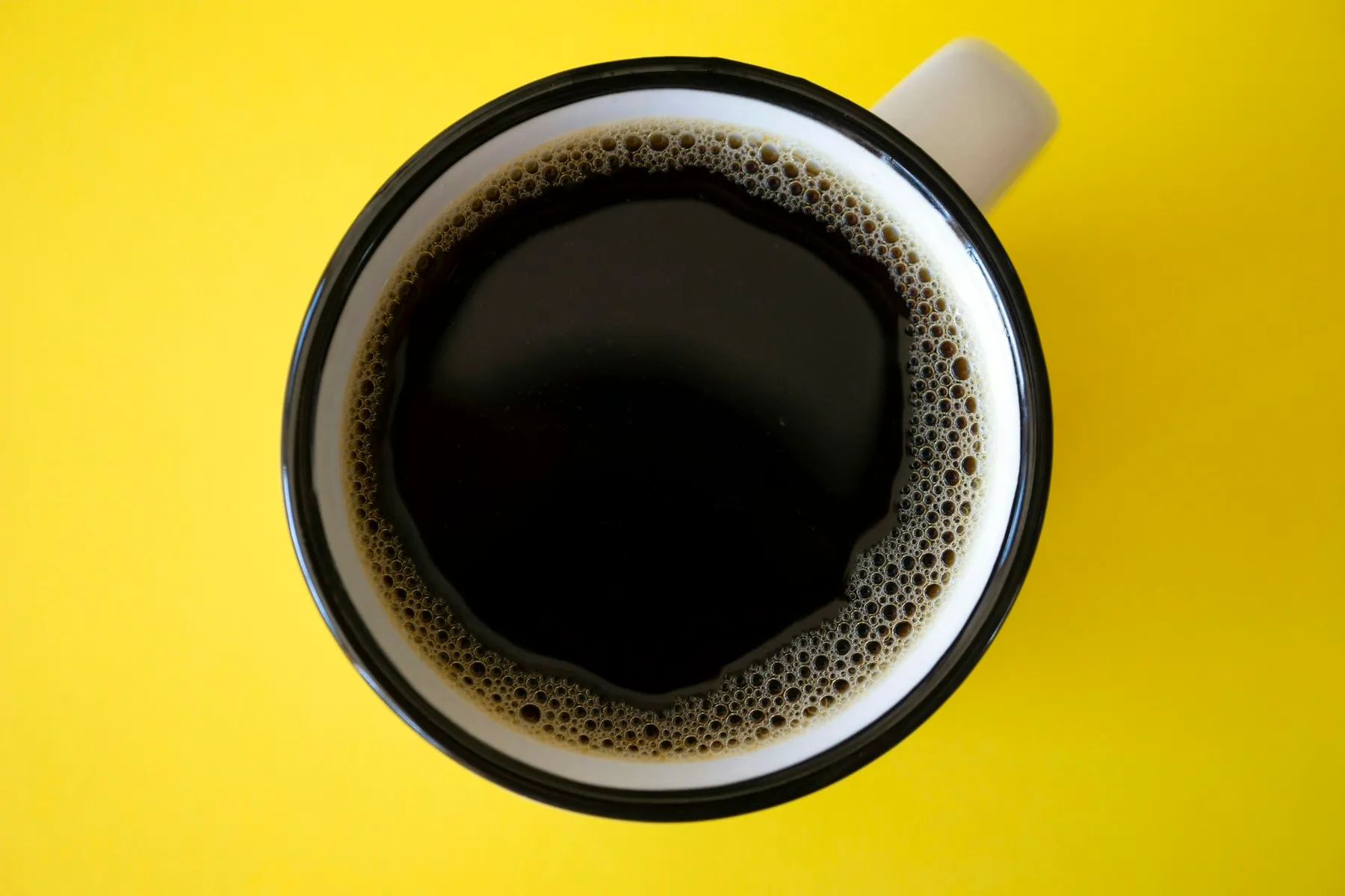 A mug of black coffee seen from above on a vivid yellow surface
