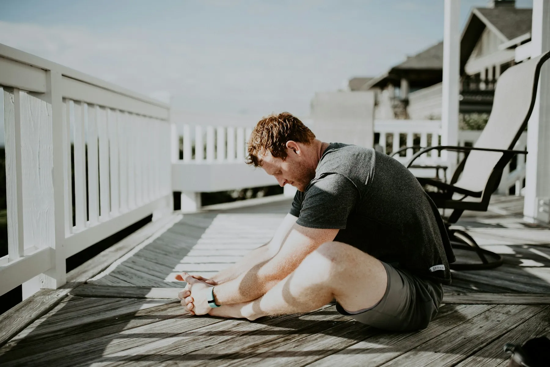 A man folding forward into a seated stretch on a wooden porch