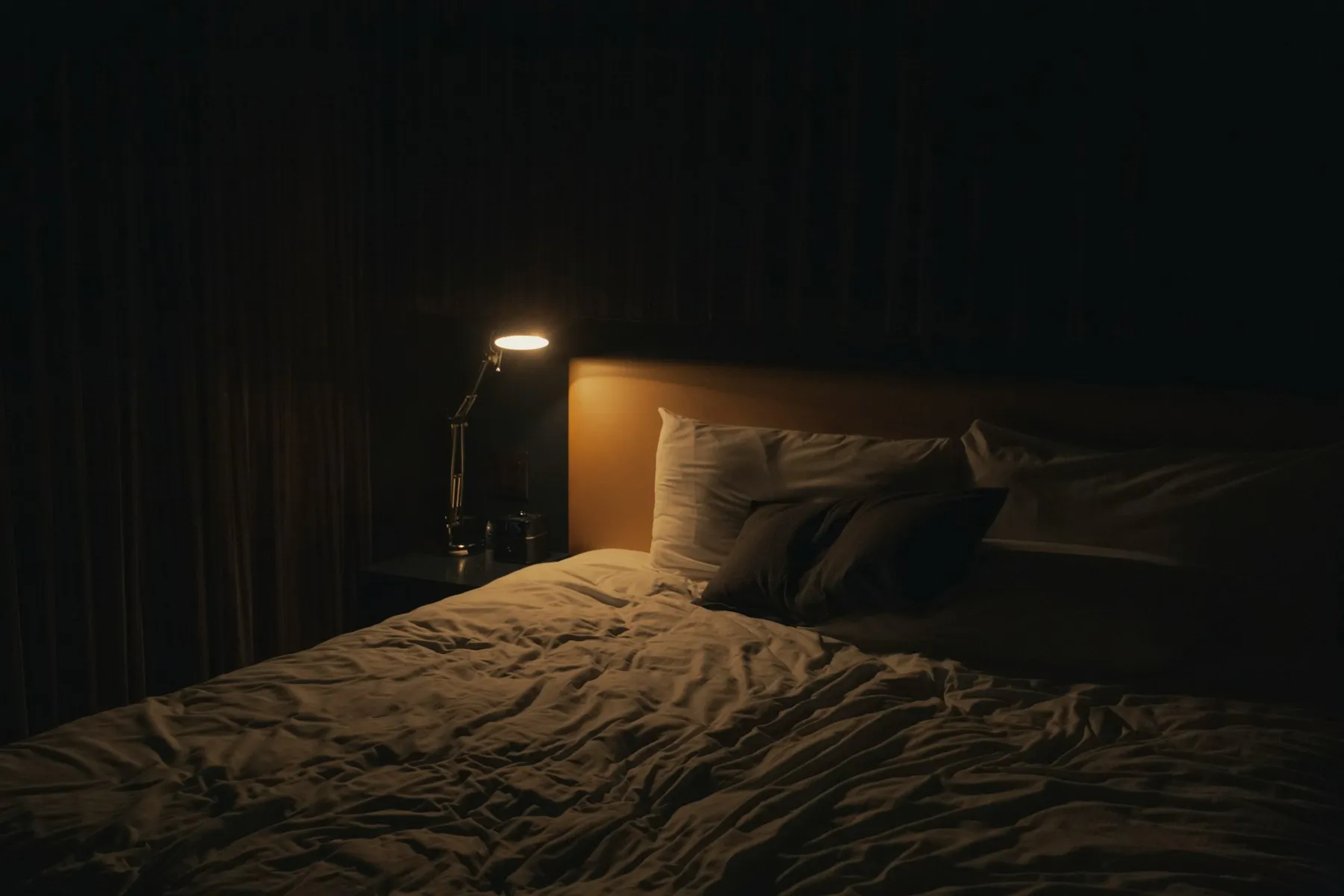 A dim bedroom with a bedside lamp switched on