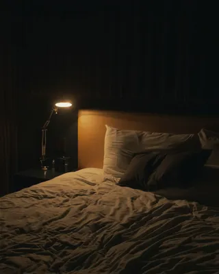 A dim bedroom with a bedside lamp switched on