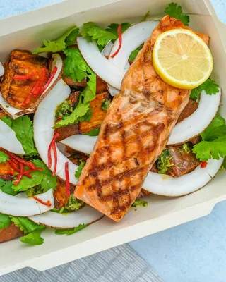 A grilled salmon fillet with lemon over roasted sweet potato, coconut, and cilantro in a takeaway box